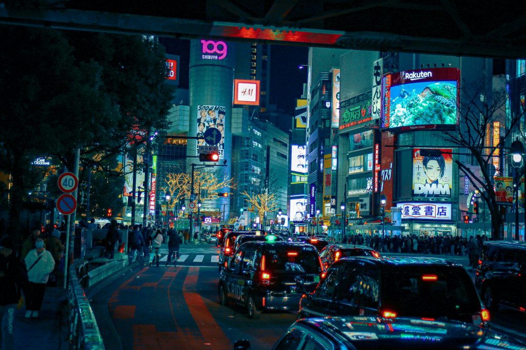 A wide shot of Shibuya Crossing at night, illuminated by neon signs and bustling crowds.